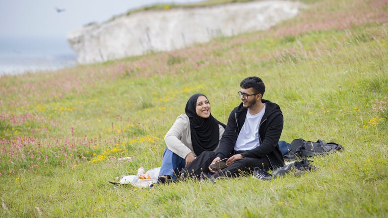 Two people sitting in a field surrounded by spring flowers on the clifftop at The White Cliffs of Dover, Kent